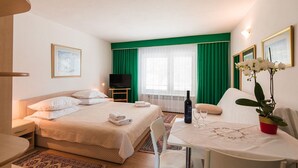 A hotel room with a bed, a TV, a table with a bottle and glasses, and a potted plant. - Cosy flat just 200 metres from the sandy beach with sea views, barbecue, air conditioning (Crikvenica)