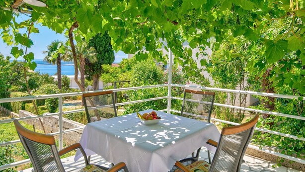 A table with a white tablecloth and chairs, set under a pergola with green grapevines. - Cosy flat just 200 metres from the sandy beach with sea views, barbecue, air conditioning (Crikvenica)
