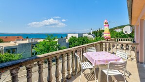 A balcony with a table and chairs, overlooking a coastal view with buildings and a lighthouse.