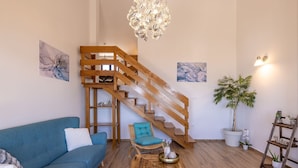 A living room with a blue sofa, a wooden staircase, a hanging light fixture, and a potted plant.