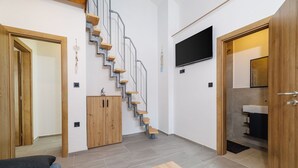 Um apartamento moderno com escada de madeira, televisão de tela plana, armário de madeira e banheiro visível através de uma porta aberta.