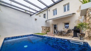 Piscina com muro de pedra e área de pátio com mobiliário de exterior.