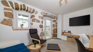 Uma sala de estar moderna com uma parede de pedra, uma poltrona preta, uma mesa de centro de madeira e uma TV fixada na parede.