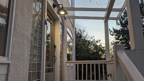 En inglasad veranda med ett trädäck, vita räcken och en dörr med glaspaneler.