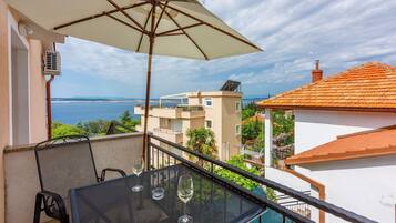 A balcony with a table and chairs, an umbrella, and a view of the sea and buildings.