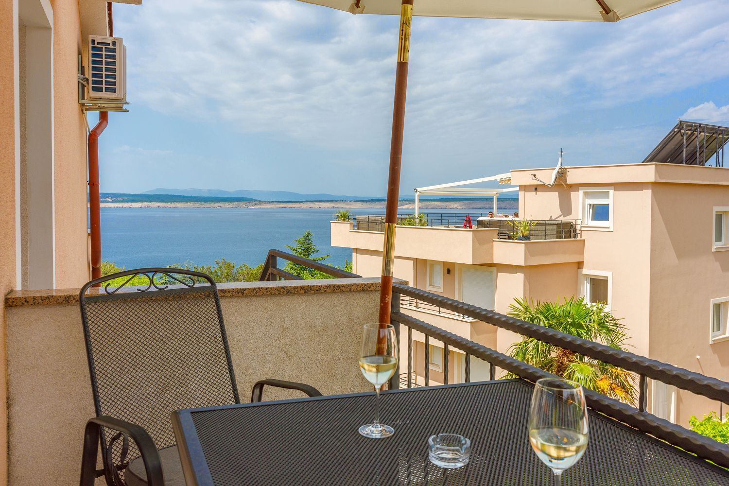 Ein Balkon mit Tisch und Stühlen, mit Blick auf ein Gewässer und ein Gebäude mit Terrasse.