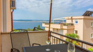Ein Balkon mit Tisch und Stühlen, mit Blick auf ein Gewässer und ein Gebäude mit Terrasse.
