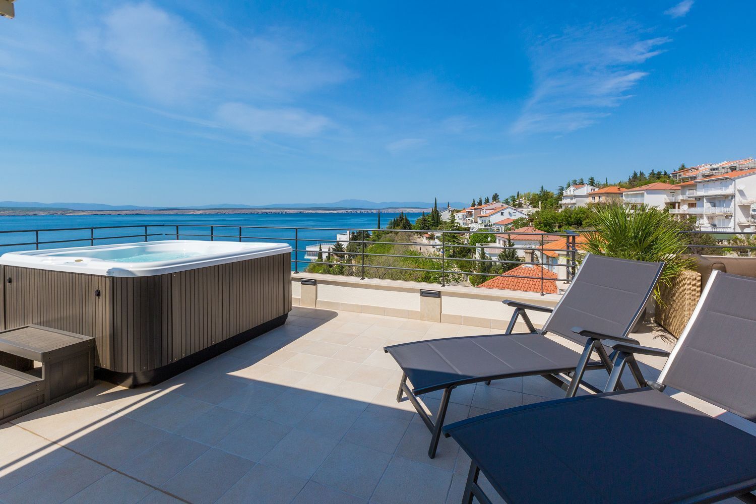 Une terrasse sur le toit équipée d’un jacuzzi, de chaises longues et offrant une vue sur la mer et les bâtiments.