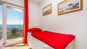 Um quarto com uma cama, uma janela com cortina vermelha e duas pinturas emolduradas na parede.