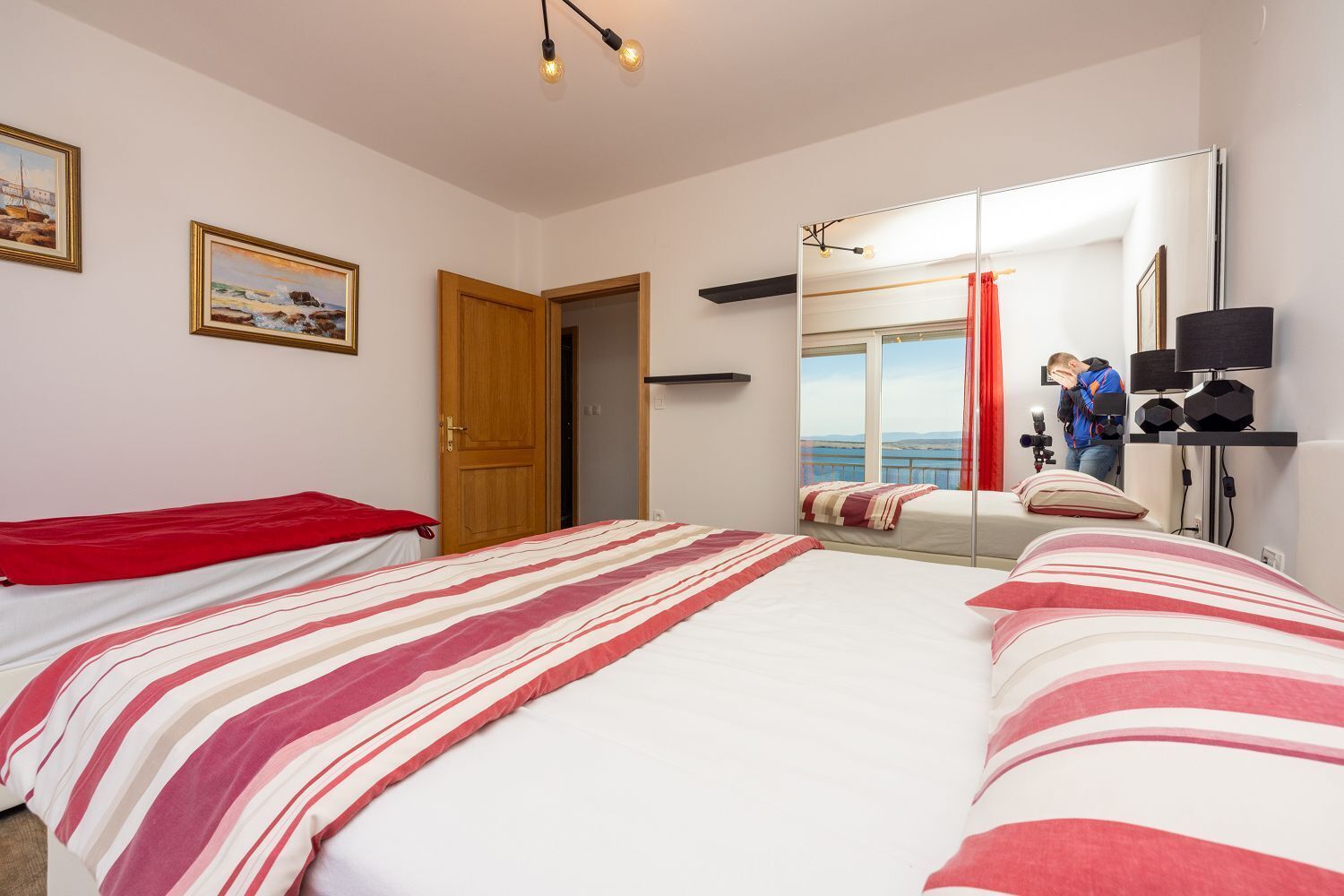 A bedroom with a large bed, a wooden door, a mirror, and a view of the sea.