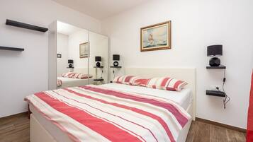 Habitación de hotel con una cama grande, una mesita de noche, un espejo, estante con lámpara y un cuadro.