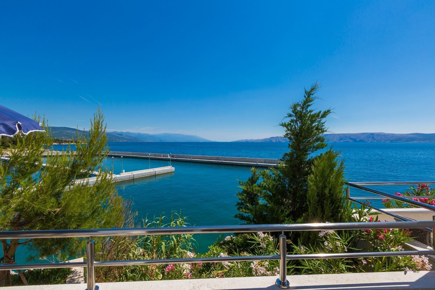 Une vue sur la côte, avec une jetée qui s’avance dans la mer, entourée de verdure et sous un ciel dégagé.
