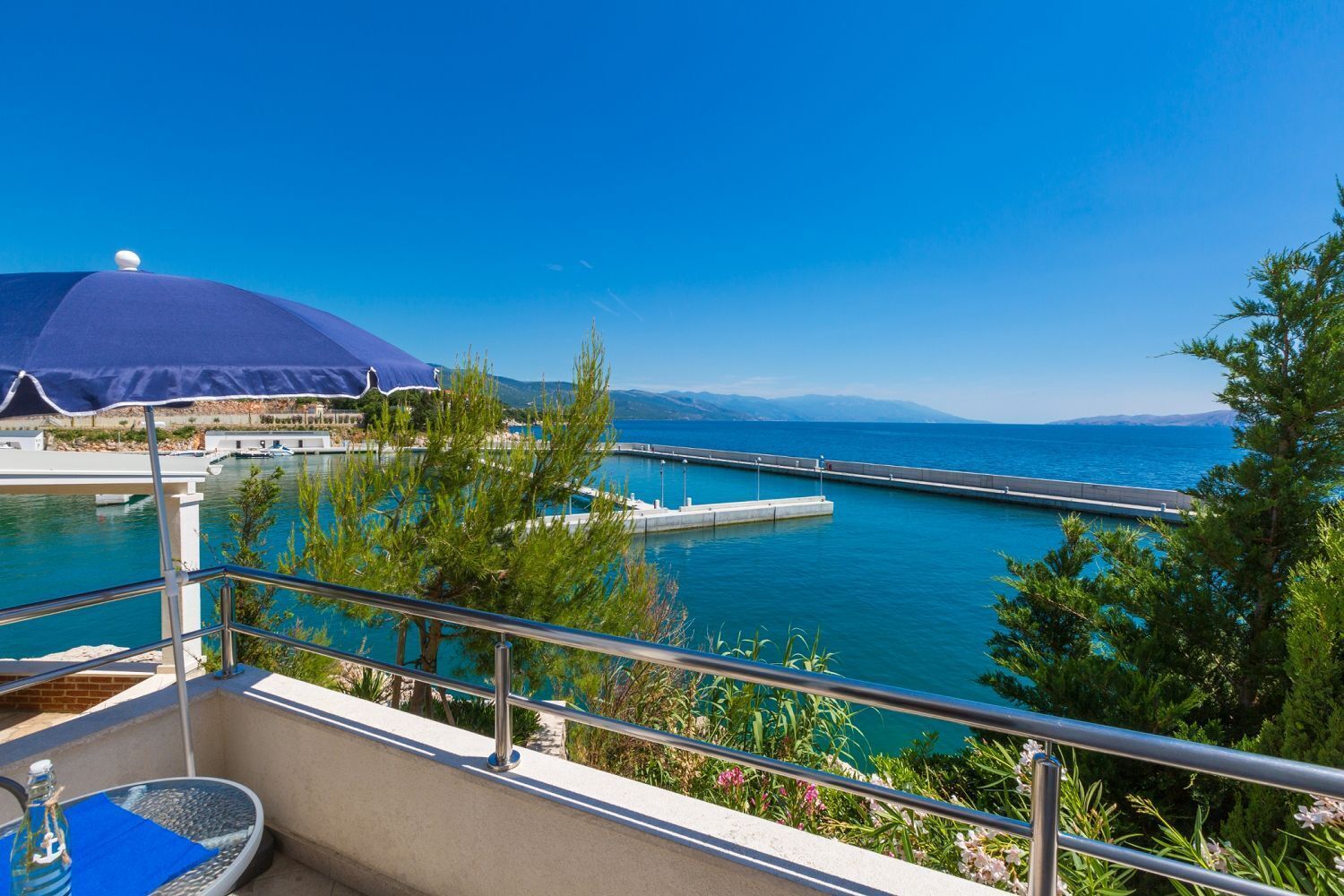A balcony with a view of a marina, a pool, and a clear blue sky.