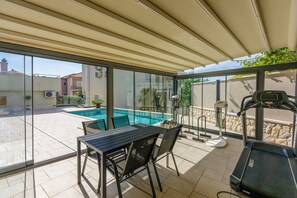 A covered outdoor area with a pool, a table with chairs, and exercise equipment.