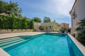 A swimming pool with clear blue water, surrounded by a stone wall and greenery.