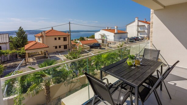 A balcony with a table and chairs, overlooking a residential area with houses and a view of the sea. - Impressive flat just 500 metres from the beach with sea views, sauna, gym, pool (Crikvenica)