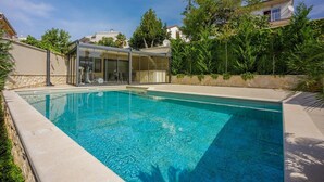 A swimming pool with a glass enclosure, surrounded by greenery and a stone wall. - Exquisite flat with sea view, sauna, gym, pool, air-conditioned bedrooms - only 500 metres to the beach (Crikvenica)