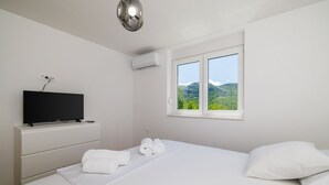 A hotel room with a bed, a flat-screen TV on a stand, a window with a mountain view, and an air conditioning unit on the wall. - Stunning villa with whirlpool, private pool, outdoor shower, fitness room, washing machine (Tribalj)