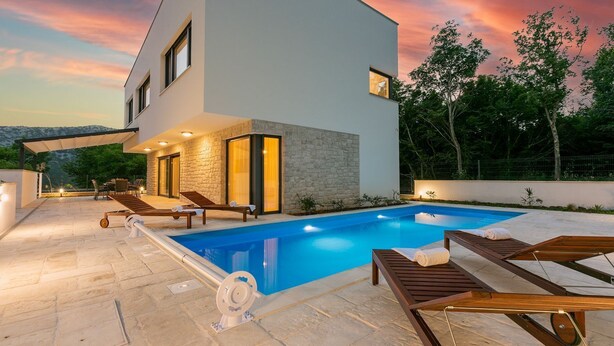 A modern two-story house with a swimming pool, outdoor seating, and a stone facade.