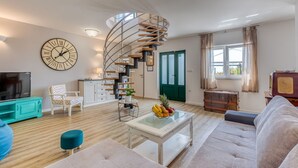 A modern living room with a spiral staircase, a large clock, a television, and a cozy seating area. - Villa Leticija (Hreljin)