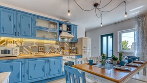 A kitchen with blue cabinets, a wooden dining table, and a window with a view. - Villa Leticija (Hreljin)