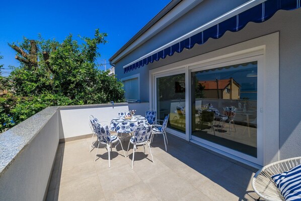 Un patio con mesa y sillas, un ventanal de vidrio que da a un balcón y vistas del entorno.