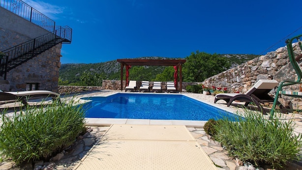 Un área de piscina con sillones de descanso, una pérgola y un edificio de piedra.