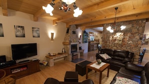 Una sala de estar acogedora con chimenea de piedra, sofás de cuero, un televisor de pantalla plana y vigas de madera en el techo.