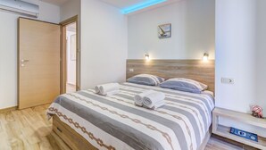 Un dormitorio con cama, mesitas de noche, luz empotrada en la pared y una puerta.