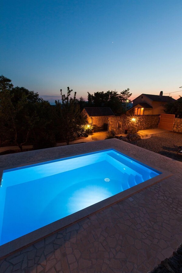 Una piscina rectangular con borde de piedra, rodeada de un patio de piedra.