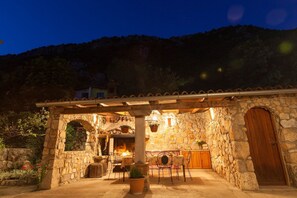 A stone building with a fireplace, outdoor seating, and a wooden door. - Rustic stone house with private pool, barbecue, terrace, loungers, outdoor shower (Grižane)