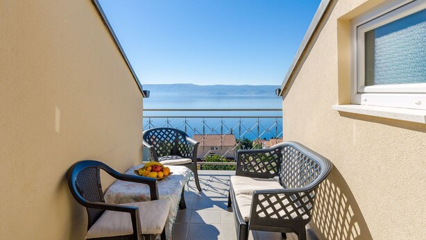 Un balcone con vista sul mare, un tavolo con sedie e una ciotola di frutta.