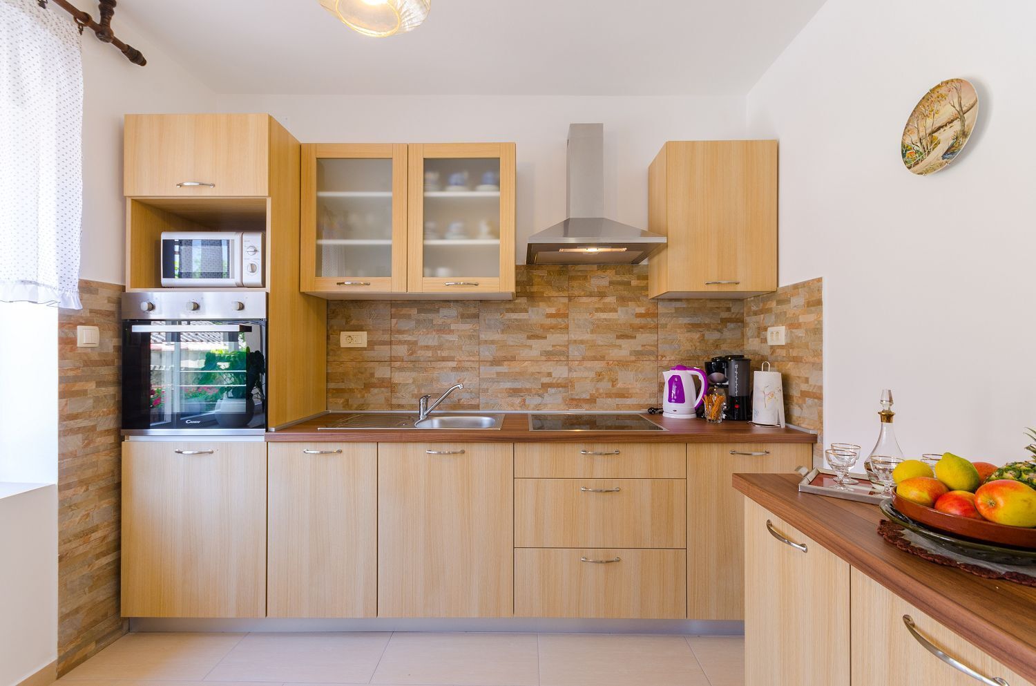 A modern kitchen with wooden cabinets, a built-in oven, a stainless steel sink, and a tiled backsplash.