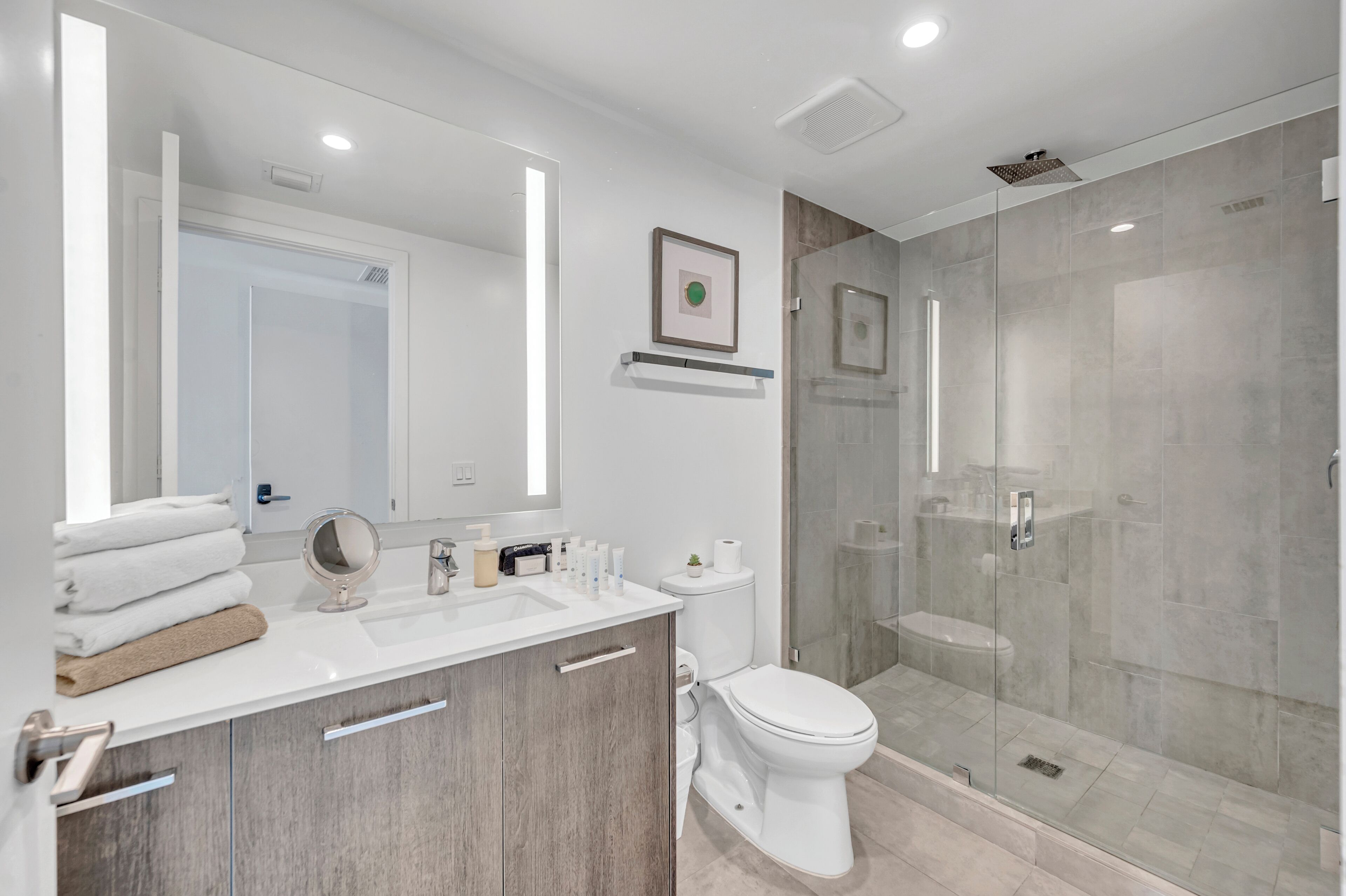 Un baño moderno con cabina de ducha de vidrio, un lavabo blanco con tocador y un inodoro.