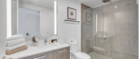 Un baño moderno con cabina de ducha de vidrio, un lavabo blanco con tocador y un inodoro.
