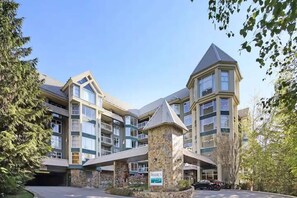 Een hotel met meerdere verdiepingen, een gevel van natuursteen, diverse balkons en een parkeerplaats.