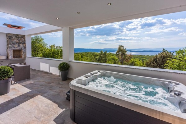 A rooftop patio with a hot tub, stone fireplace, and a view of the ocean.