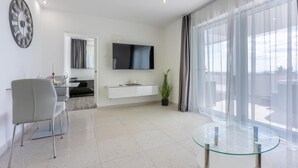 Un saló modern amb una taula de vidre, un televisor de pantalla plana, zona de menjador amb cadires i una finestra gran amb cortines.