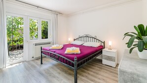 Ein Schlafzimmer mit einem Metallbettgestell, einer violetten Bettdecke, weißen Kissen, einem Nachttisch mit Lampe und einem Blumentopf.