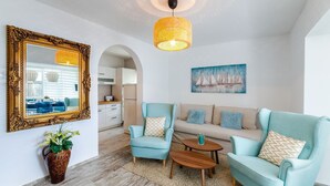 Una sala de estar moderna con un sofá azul claro, dos sillones a juego, una mesa de centro de madera, un espejo decorativo y una lámpara de techo.