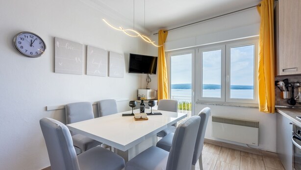 Una cocina moderna con comedor, ventanas amplias con vistas, televisión de pantalla plana y un reloj en la pared.