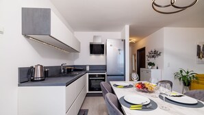 A modern kitchen with a built-in oven, a refrigerator, and a dining area with a marble table set for two. - Light-flooded flat with sea view, private balcony, WiFi, private car park (Crikvenica)