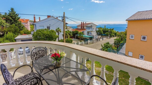 Un balcon avec une table et des chaises, donnant sur une ville côtière avec ses maisons et offrant une vue sur la mer.
