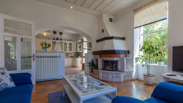A spacious living room with a fireplace, blue sofas, and a kitchen area visible through an archway.