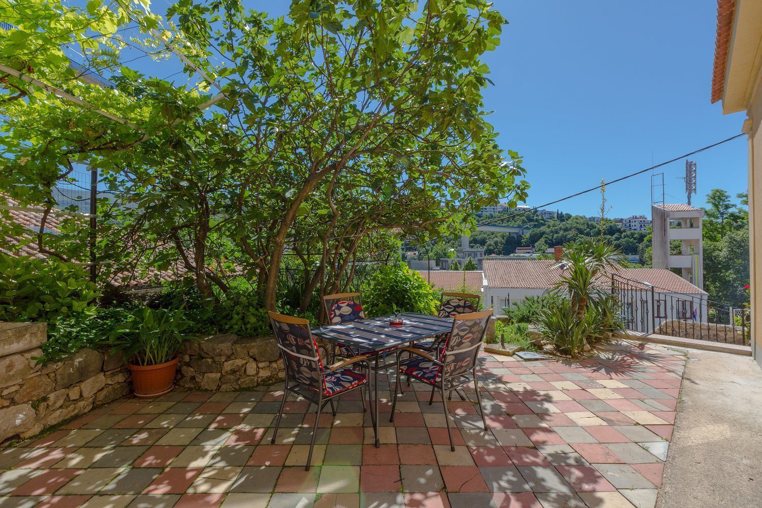 An outdoor patio with a table and chairs, surrounded by greenery and a stone wall.