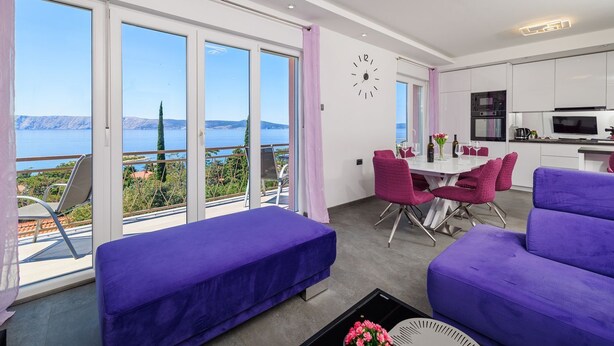 Eine moderne Wohnung mit Balkon und Blick auf eine reizvolle Landschaft, einem Essbereich mit violetten Möbeln und einer Küche mit weißen Schränken.