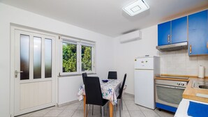 A compact kitchen with a dining area, featuring a refrigerator, oven, and a window with a view of greenery.