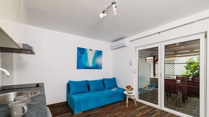 Eine moderne Küche mit einem blauen Sofa, einem kleinen Tisch mit einer Vase und Blick auf einen Außenbereich mit Essplatz durch Glastüren.