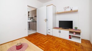 Kompakti oleskelutila, jossa on pieni keittiönurkkaus, televisio ja pieni hylly koriste-esineille.