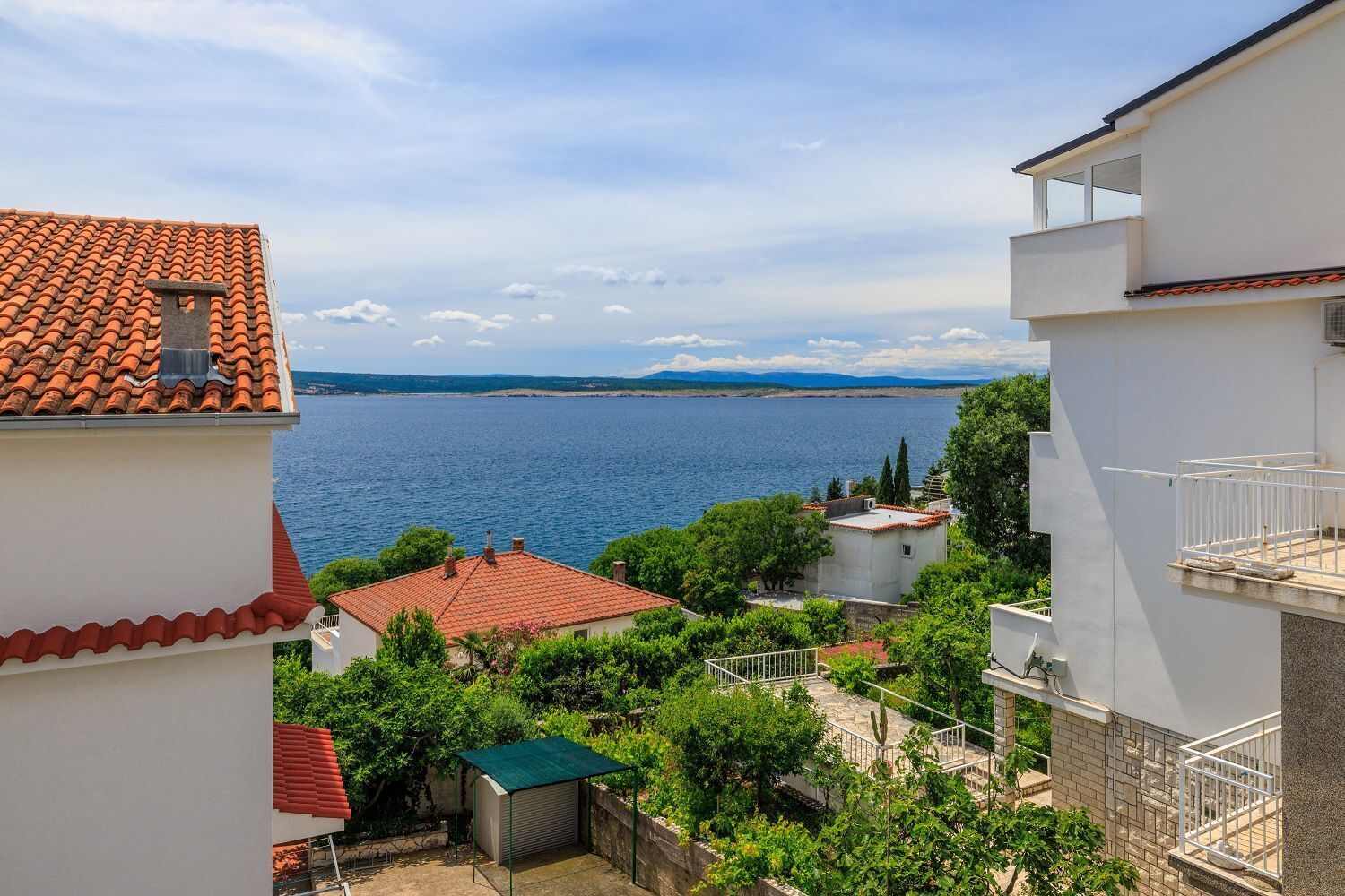 A coastal residential area with terracotta-tiled roofs, white buildings, and a view of the sea.